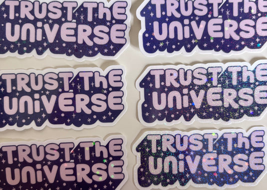 Six die-cut stickers featuring the phrase 'TRUST THE UNIVERSE' in light pink bubble letters over a dark purple glittery starry space background, arranged on a light beige surface.